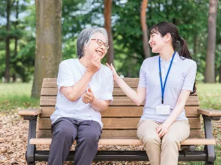 介護士と高齢女性がベンチで笑顔で会話している様子